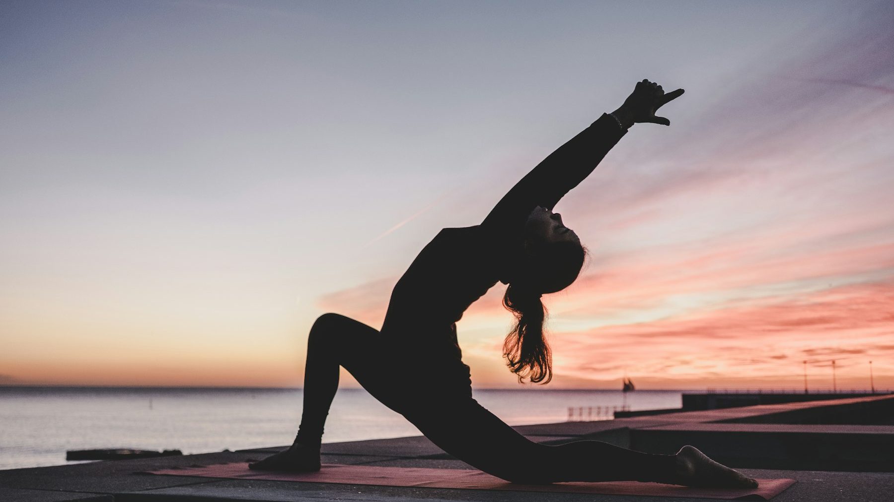 Silueta de una mujer practicando yoga al atardecer junto al mar